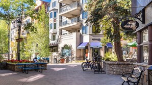Un'area pedonale pavimentata con panchine, un rastrello per biciclette e un edificio con il cartello 'Alpine Pizza Company'.