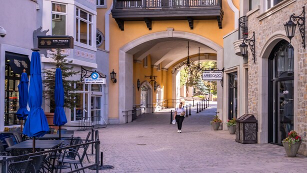 Una strada acciottolata con tavoli all'aperto, un edificio giallo con balconi e un arco.