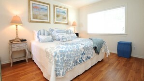 A bedroom with a large bed, two bedside lamps, a window, and two framed pictures on the wall.