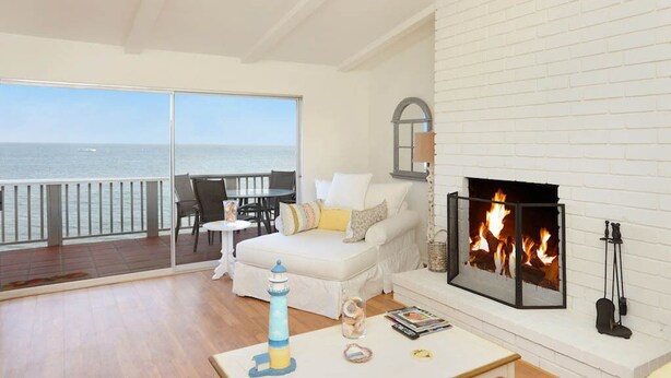 A spacious living room with a white brick fireplace, a white sofa, and a view of the ocean through large sliding glass doors.