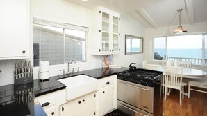 A modern kitchen with white cabinetry, a black countertop, and a view of the ocean.