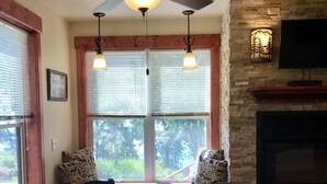 A dining area with a round table, chairs, a fireplace, and large windows with blinds.