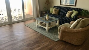 A living room with a striped sofa, a glass coffee table, and a wicker chair. - Ocean Front+Spacious living+Dog Friendly+Best Views+Pools+CB Pier+Freeman Park (Carolina Beach)