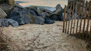 A beach with large rocks and a wooden fence. - Ocean Front+Spacious living+Dog Friendly+Best Views+Pools+CB Pier+Freeman Park (Carolina Beach)