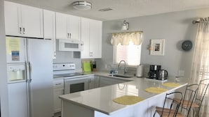 A modern kitchen with white cabinetry, a central island with bar stools, a built-in oven, and a microwave. - Ocean Front+Spacious living+Dog Friendly+Best Views+Pools+CB Pier+Freeman Park (Carolina Beach)