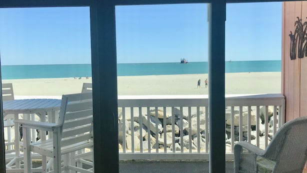 A beach view from a covered area with white chairs and a wicker rocking chair. - Ocean Front+Spacious living+Dog Friendly+Best Views+Pools+CB Pier+Freeman Park (Carolina Beach)