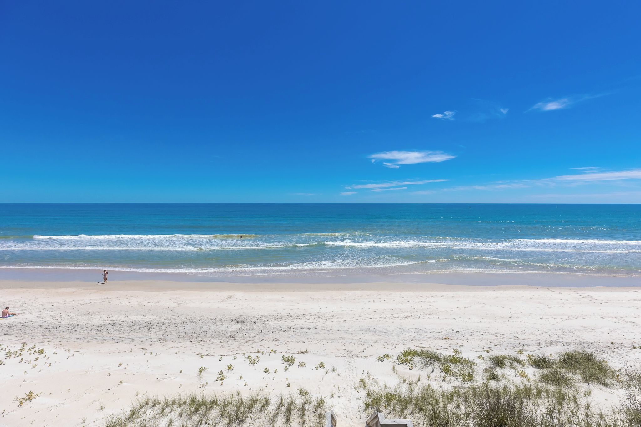 A beach with a clear sky, sandy shore, and a few people.