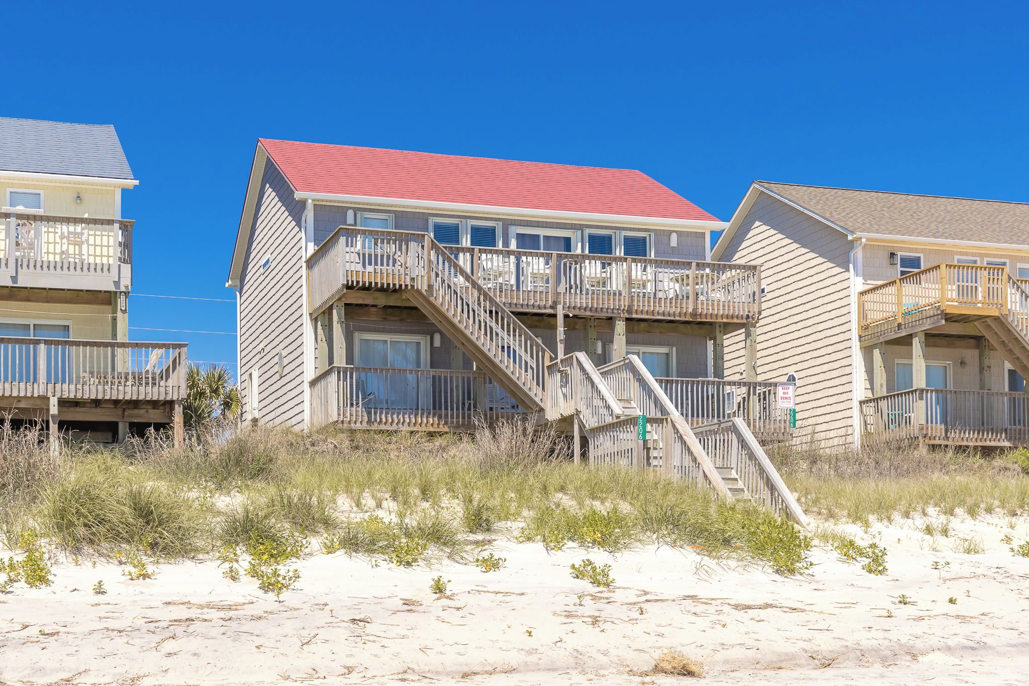 A beachfront building with multiple balconies, a red roof, and a staircase leading to the upper levels.