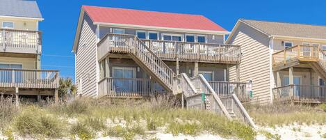 A beachfront building with multiple balconies, a red roof, and a staircase leading to the upper levels.