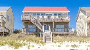 A beachfront building with a red roof, multiple balconies, and a wooden staircase leading to the entrance. - C' Turtle - 5 BR Oceanfront Home - Elevator, Spectacular Views from Decks (Surf City)