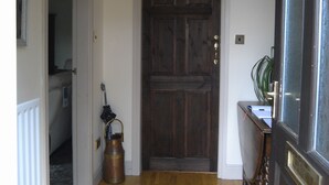 Un couloir avec une porte en bois, un radiateur, une plante et un luminaire suspendu.