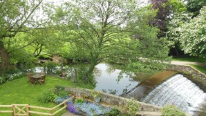 Un jardin paisible avec un bassin, une table en bois entourée de chaises et un mur de pierre orné de fleurs.