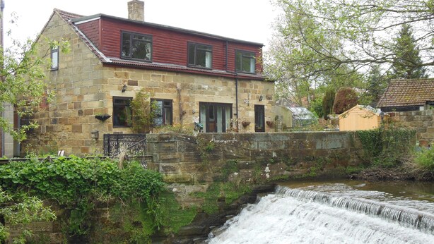 Un bâtiment en pierre avec un toit rouge, une petite cascade et un jardin.