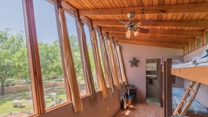 Une chambre avec un lit superposé, un ventilateur de plafond et de grandes fenêtres donnant sur un jardin.
