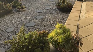 Un espace jardin aménagé avec des allées de gravier, des plantes en pot et un bâtiment en arrière-plan.