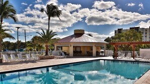 A swimming pool with lounge chairs and a covered seating area, surrounded by palm trees and a clear sky. - Waterfront Islamorada Condo – Heated Pool, Marina & Deeded Boat Slip (Tavernier)