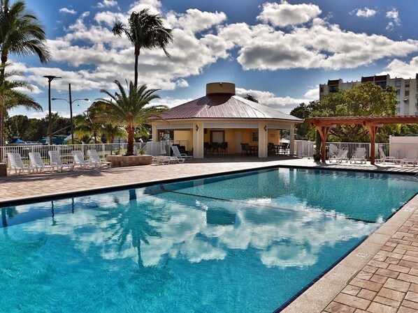 A swimming pool with lounge chairs and a covered seating area, surrounded by palm trees and a clear sky. - Futura Yacht Club Islamorada Condo – Heated Pool, Marina & Deeded Slip (Tavernier)