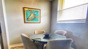 A dining area with a round table, four chairs, a ceiling fan, and a framed artwork on the wall. - Waterfront Islamorada Condo – Heated Pool, Marina & Deeded Boat Slip (Tavernier)