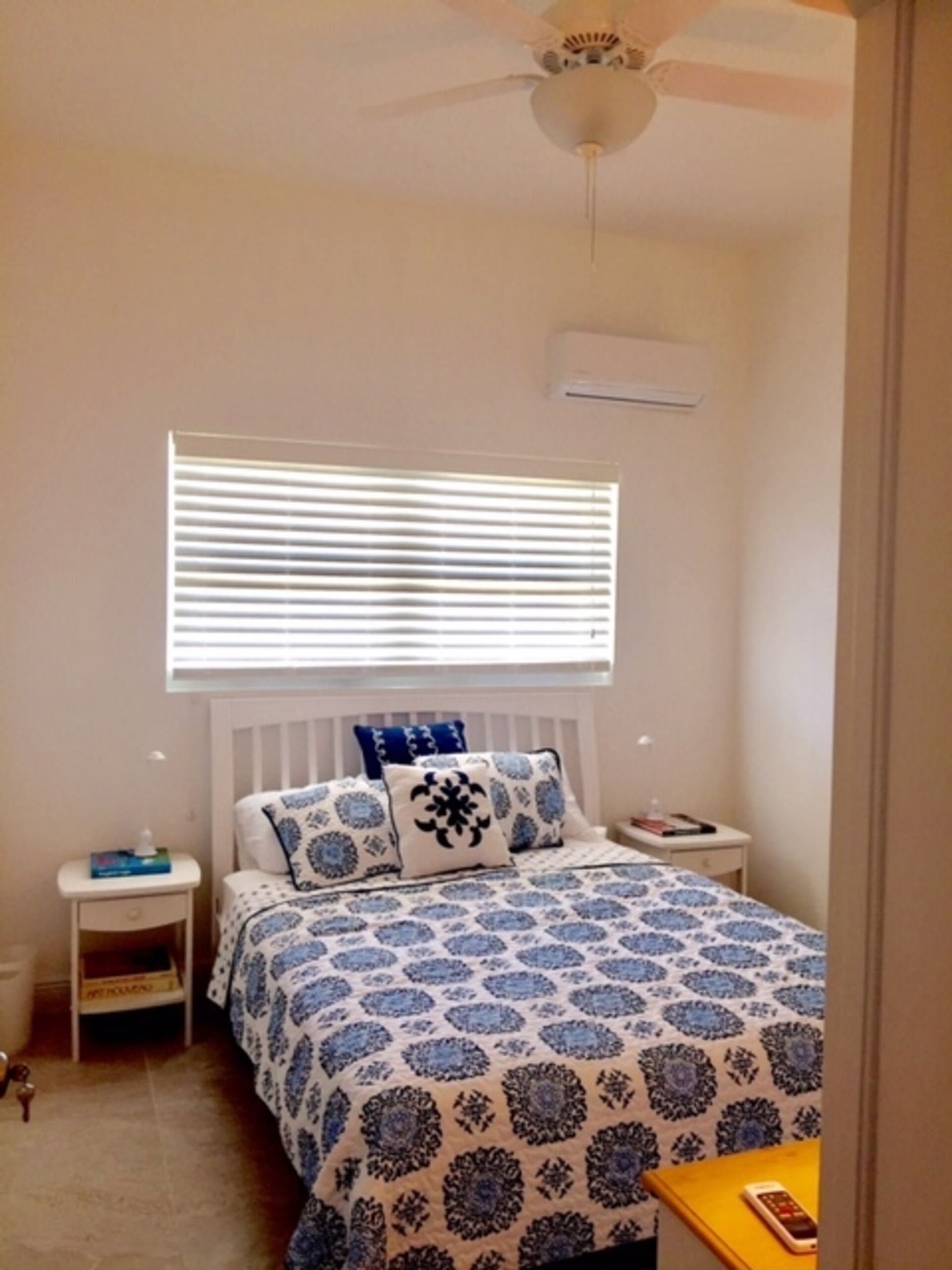 Une chambre à coucher comprenant un lit, une table de chevet, une commode, une fenêtre avec des stores et un ventilateur de plafond.