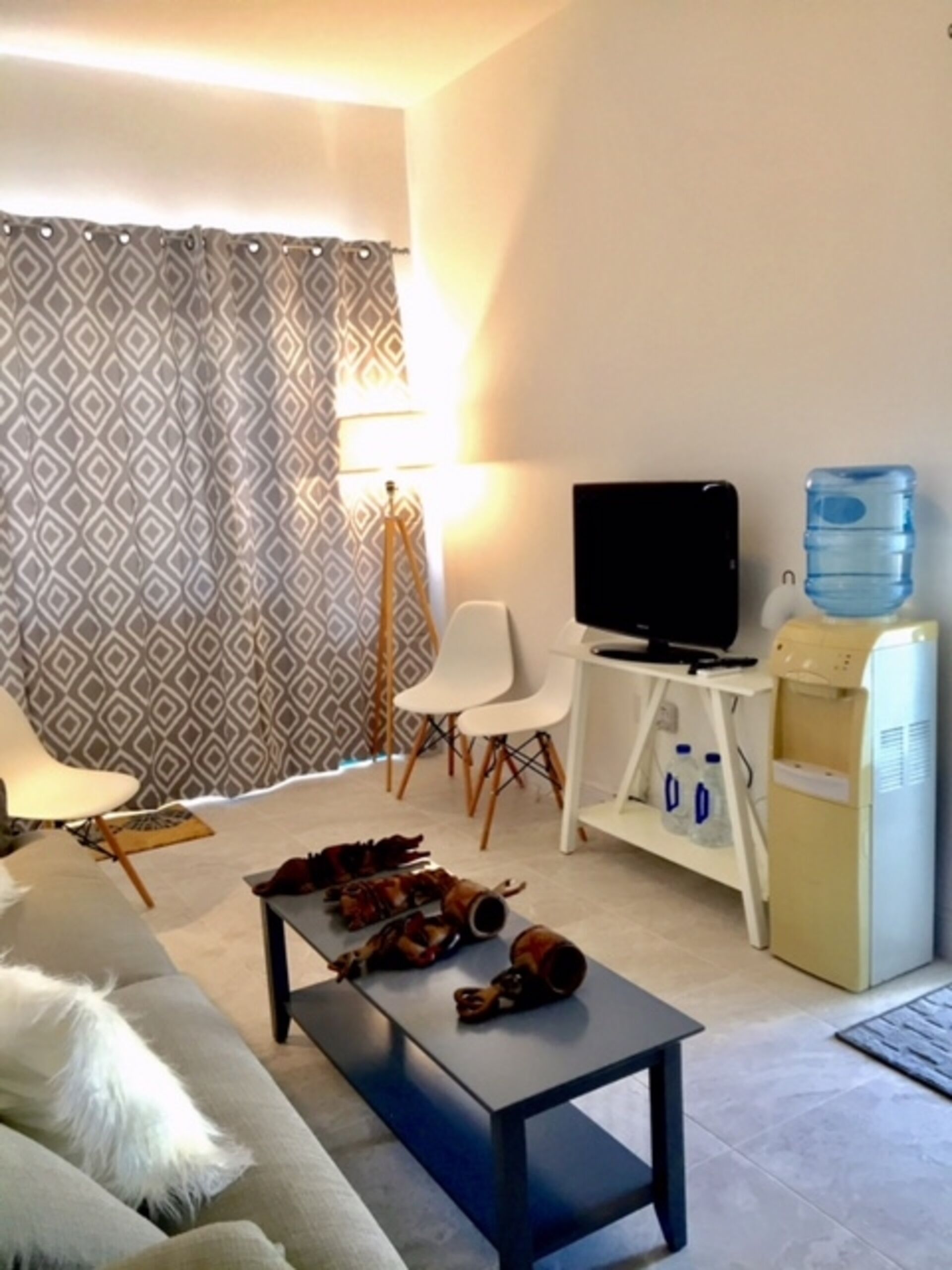 Ein Wohnzimmer mit einer Couch, einem Couchtisch, einem Fernseher auf einem Schrank, einem Wasserspender und einer Lampe.
