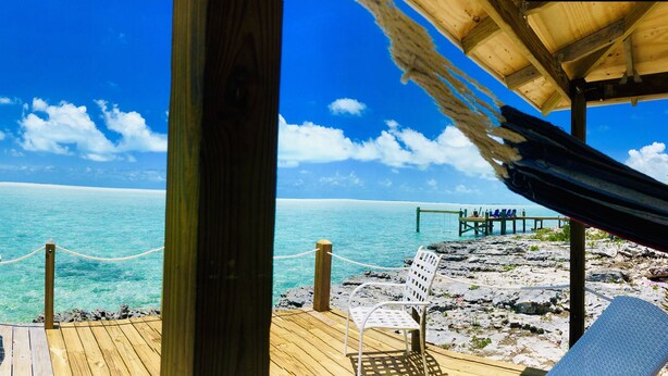 A wooden deck with a rope barrier, white lounge chairs, and a table. - Bonefish Bungalow is the perfect haven for eager fishing enthusiasts (Georgetown)