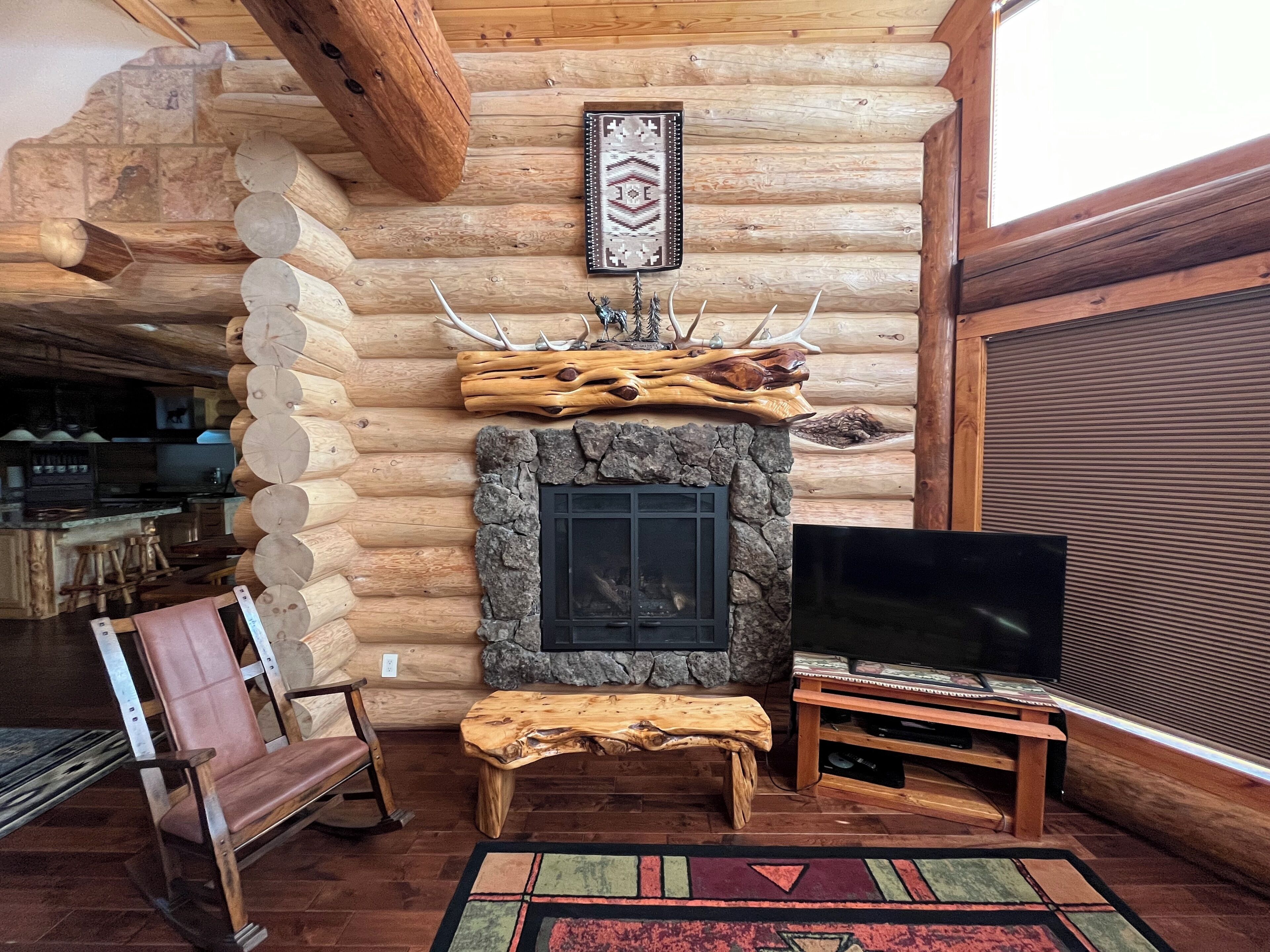 L’intérieur d’un chalet en rondins, avec une cheminée en pierre, des bancs en bois, un téléviseur et un coin repas.