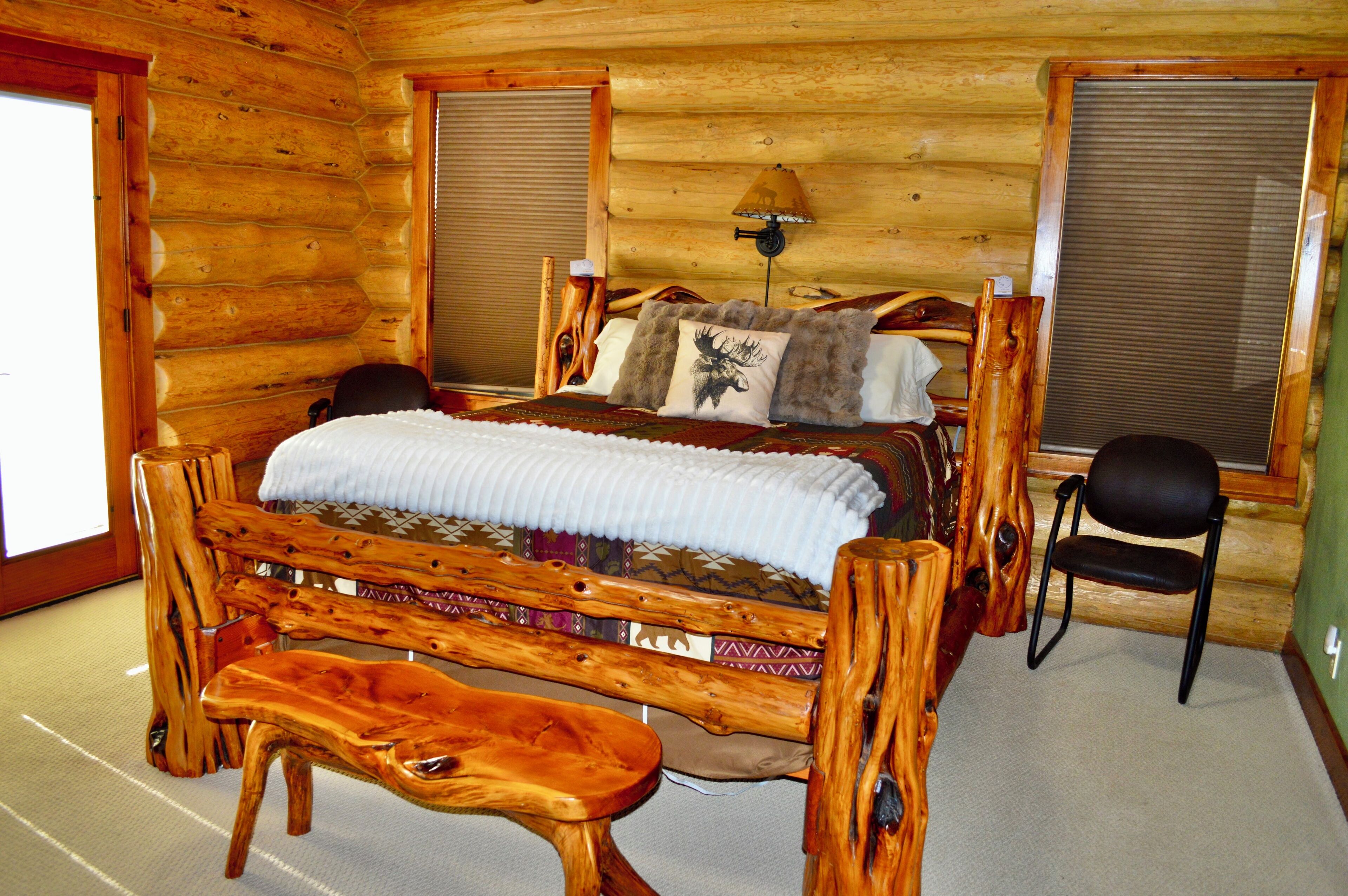 A log cabin bedroom with a wooden bed, a bench, a chair, and a lamp.