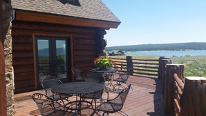 Eine Holzhütte mit einer Terrasse, Sitzgelegenheiten im Freien und Blick auf einen See und Berge.
