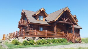 Eine Blockhütte mit Steinuntergrund, Holzterrasse und einer Treppe zum Eingang.