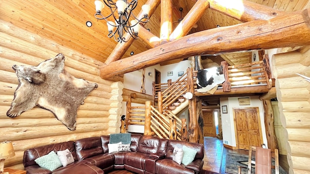 Ein Blockhaus-Interieur mit Ledersofa, einem Chandelier, einem aufgehängten Tierfell und einer Holztreppe.