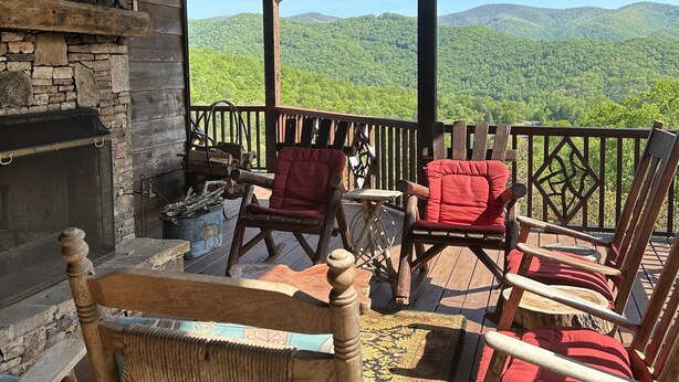 Une terrasse en bois, dotée de chaises en osier et d’une cheminée, qui offre une vue sur un paysage montagneux.