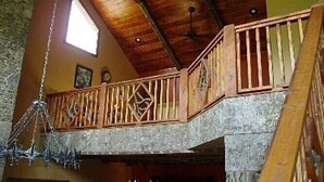 Un intérieur rustique avec un escalier en bois, un balcon doté d’une balustrade et un lustre suspendu.