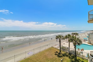 A beach view with a fenced area, a pool, and palm trees. - COV 220 - Elegant Oceanfront Villa - Unbeatable Views - 2 Pools (Folly Beach)