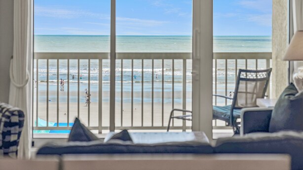 Una habitación con vista al mar, un balcón con barandilla y una silla.