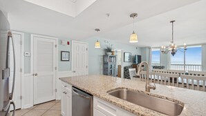 Cocina con encimera de granito, pileta de acero inoxidable, muebles blancos y vista al océano a través de amplias ventanas.