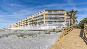 Un hotel frente a la playa con varios balcones, un paseo marítimo de madera y una playa de arena.