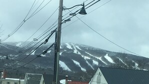 A snow-covered street with houses, a truck, and a mountain in the background. - Okemo Mt. Family Affordable 1st floor, village shuttle, walk to town, Dogs OK  (Ludlow)