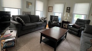 A living room with a grey sofa, a wooden coffee table, a black armchair, and a TV on a stand. - Okemo Mt. Family Affordable 1st floor, village shuttle, walk to town, Dogs OK  (Ludlow)