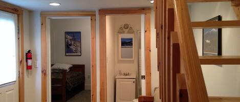 A wooden staircase leading to a bedroom with a bed, a small bathroom, and a hallway with a fire extinguisher.