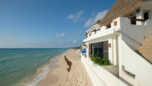 Een hotel aan het strand met rieten dak, een zandstrand en helderblauw water.