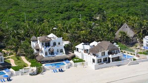 Een strandhuis met meerdere gebouwen, een zwembad en een strandgedeelte met ligbedden.
