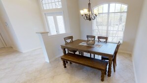 A dining area with a wooden table and chairs, a chandelier, and a window with blinds. - Sunny Pool & Spa inside Lanai! Dock and Water access! 3bd 2bath home. (Marco Island)