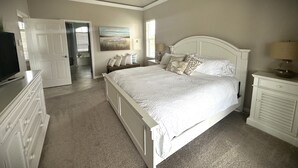 A bedroom with a large bed, a dresser, a television, and a door leading to a bathroom. - Sunny Pool & Spa inside Lanai! Dock and Water access! 3bd 2bath home. (Marco Island)