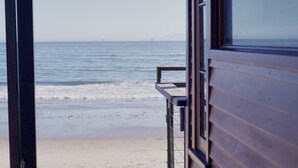 Uitzicht op het strand vanaf een houten gebouw met een raam dat uitkijkt over de oceaan.