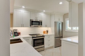 A modern kitchen with white cabinets, stainless steel appliances, and a marble countertop.