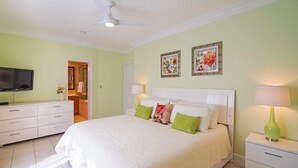 A bedroom with a bed, bedside tables, a television, and a ceiling fan. - Regal Beach Club #614 (Seven Mile Beach)