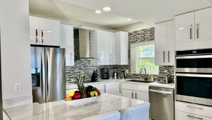 A modern kitchen with white cabinetry, stainless steel appliances, and a marble countertop. - Regal Beach Club #614 (Seven Mile Beach)
