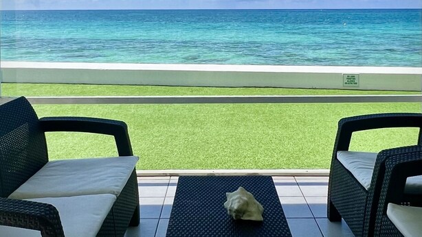 A balcony with two wicker chairs, a small table, and a view of the ocean. - Regal Beach Club #614 (Seven Mile Beach)