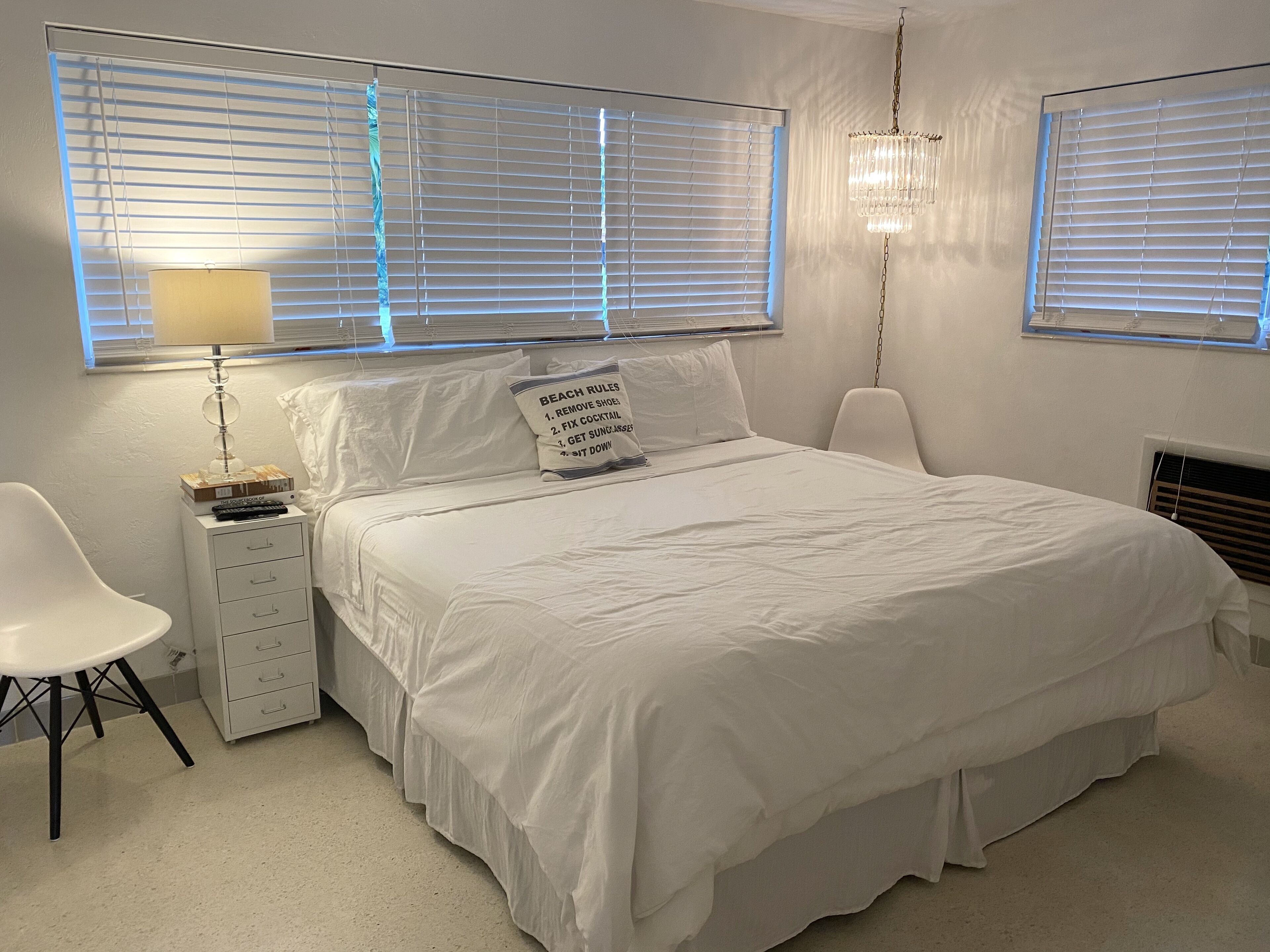 Een slaapkamer met een bed, nachtkastje, stoel en raam met jaloezieën.