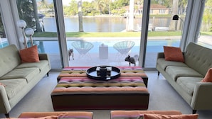 Un salon moderne doté d’une grande fenêtre, offrant une vue sur la piscine, et d’un coin repas avec une table basse.
